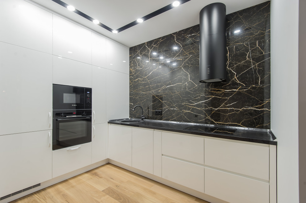 Photo of a mid-sized contemporary l-shaped kitchen in Moscow with a drop-in sink, flat-panel cabinets, white cabinets, black splashback, porcelain splashback, panelled appliances, no island, beige floor and black benchtop.