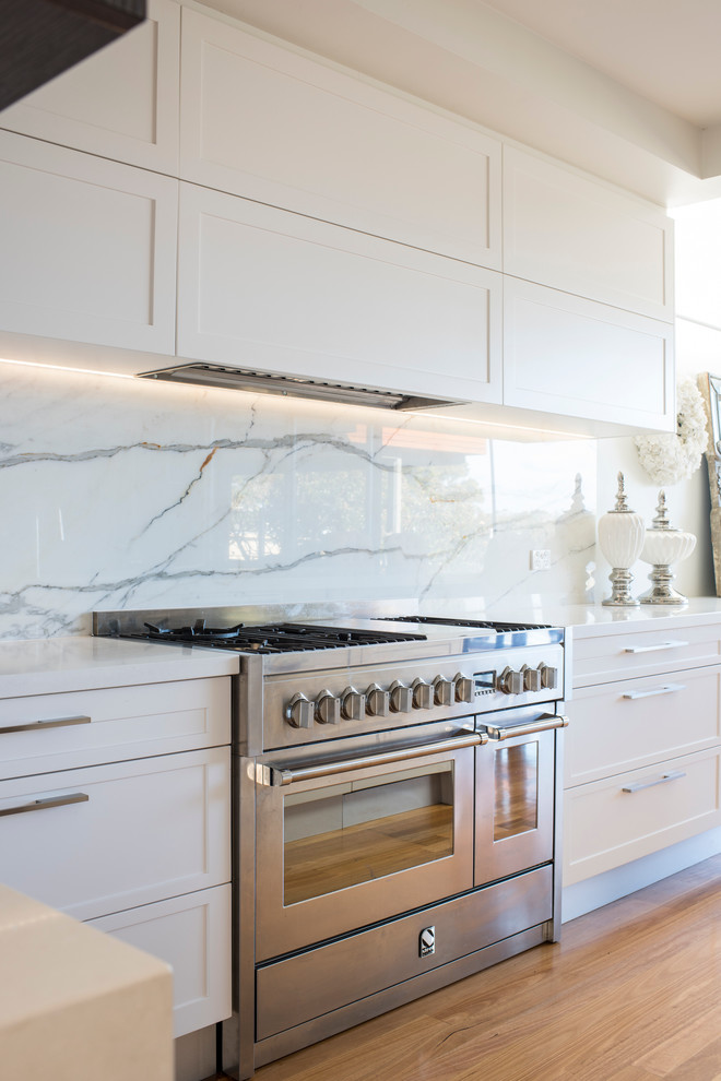 Design ideas for a large traditional l-shaped open plan kitchen in Central Coast with an undermount sink, shaker cabinets, white cabinets, quartz benchtops, white splashback, stone slab splashback, stainless steel appliances, light hardwood floors and with island.