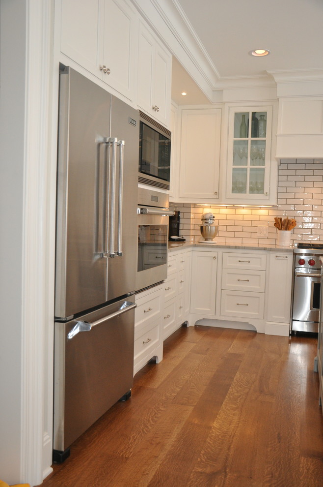 Inspiration for a large transitional l-shaped medium tone wood floor and brown floor open concept kitchen remodel in Cleveland with an undermount sink, recessed-panel cabinets, white cabinets, marble countertops, white backsplash, subway tile backsplash, stainless steel appliances, an island and white countertops