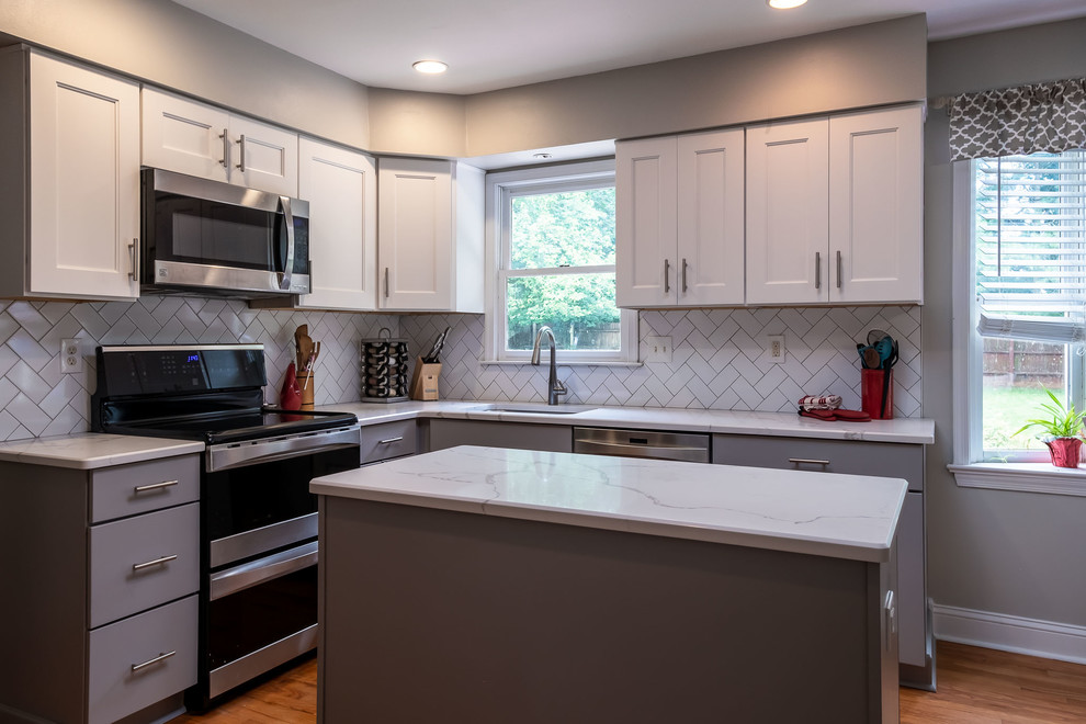 Photo of a mid-sized contemporary galley separate kitchen in Philadelphia with an undermount sink, recessed-panel cabinets, white cabinets, quartz benchtops, white splashback, cement tile splashback, stainless steel appliances, medium hardwood floors, with island, brown floor and white benchtop.