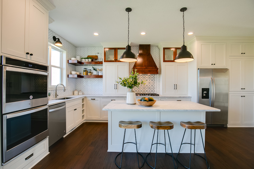 Transitional l-shaped kitchen in Minneapolis with an undermount sink, shaker cabinets, white cabinets, white splashback, stainless steel appliances, dark hardwood floors, with island, brown floor and white benchtop.