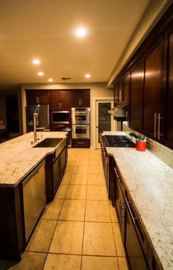 Inspiration for a large transitional l-shaped ceramic tile eat-in kitchen remodel with a farmhouse sink, shaker cabinets, brown cabinets, granite countertops, green backsplash, subway tile backsplash, stainless steel appliances and an island