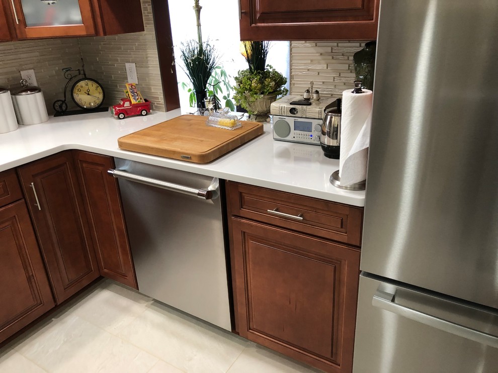 Photo of a mid-sized traditional l-shaped kitchen pantry in New York with an undermount sink, raised-panel cabinets, medium wood cabinets, quartz benchtops, grey splashback, glass tile splashback, stainless steel appliances, ceramic floors, no island, white floor and white benchtop.