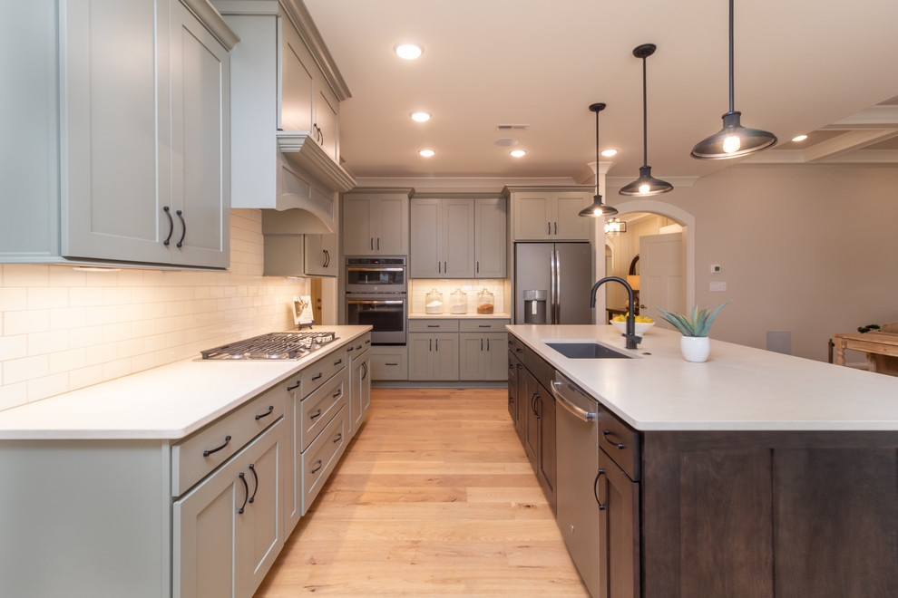 Open concept kitchen - mid-sized transitional l-shaped open concept kitchen idea with an undermount sink, shaker cabinets, quartz countertops, white backsplash, subway tile backsplash, stainless steel appliances, an island and white countertops
