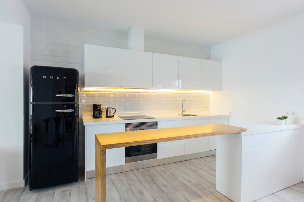 Inspiration for a mid-sized modern galley open plan kitchen in Palma de Mallorca with flat-panel cabinets, white cabinets, white splashback, subway tile splashback, black appliances and a peninsula.