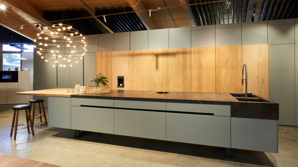 Свежая идея для дизайна: огромная параллельная кухня-гостиная в современном стиле с плоскими фасадами, светлыми деревянными фасадами, бетонным полом, островом и черной столешницей - отличное фото интерьера