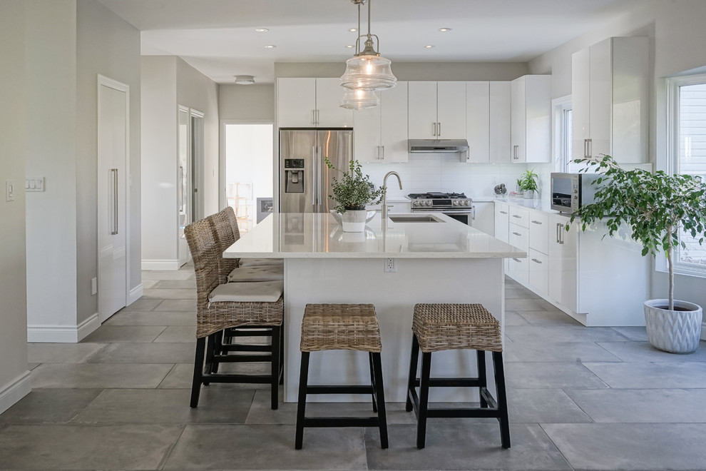 Example of a large transitional l-shaped gray floor open concept kitchen design in Montreal with flat-panel cabinets, white cabinets, white backsplash, ceramic backsplash, stainless steel appliances, an island, white countertops and an undermount sink