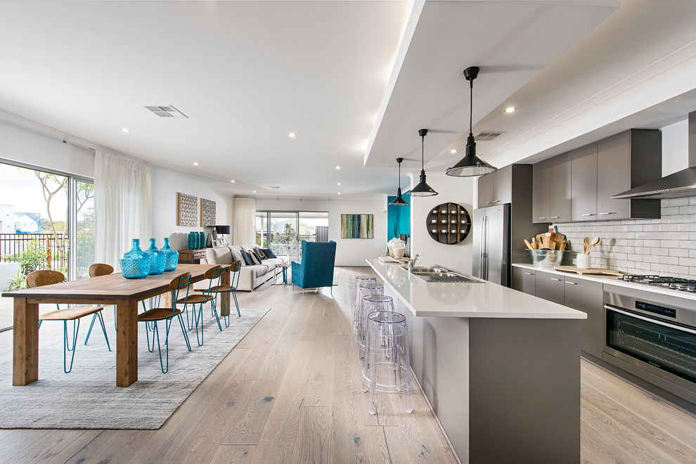 This is an example of a beach style open plan kitchen in Perth with a drop-in sink, flat-panel cabinets, grey cabinets, white splashback, stainless steel appliances, medium hardwood floors and with island.