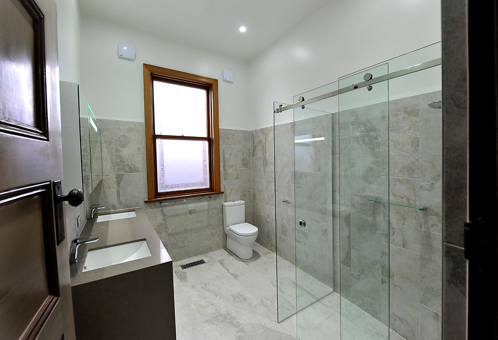 Photo of a mid-sized contemporary master bathroom in Melbourne with beige cabinets, a double shower, a two-piece toilet, beige tile, stone slab, beige walls, porcelain floors, an undermount sink and glass benchtops.