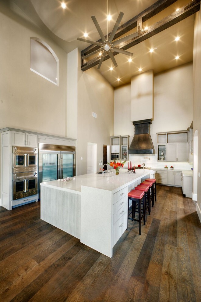 Example of a large transitional u-shaped medium tone wood floor eat-in kitchen design in Sacramento with a farmhouse sink, white cabinets, solid surface countertops, white backsplash, subway tile backsplash, stainless steel appliances, an island and shaker cabinets
