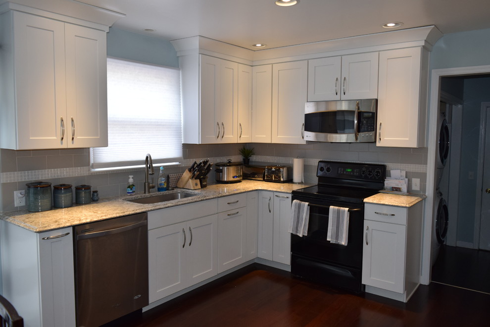 Kitchen - transitional l-shaped dark wood floor kitchen idea with shaker cabinets, white cabinets, quartz countertops, gray backsplash, glass tile backsplash and black appliances