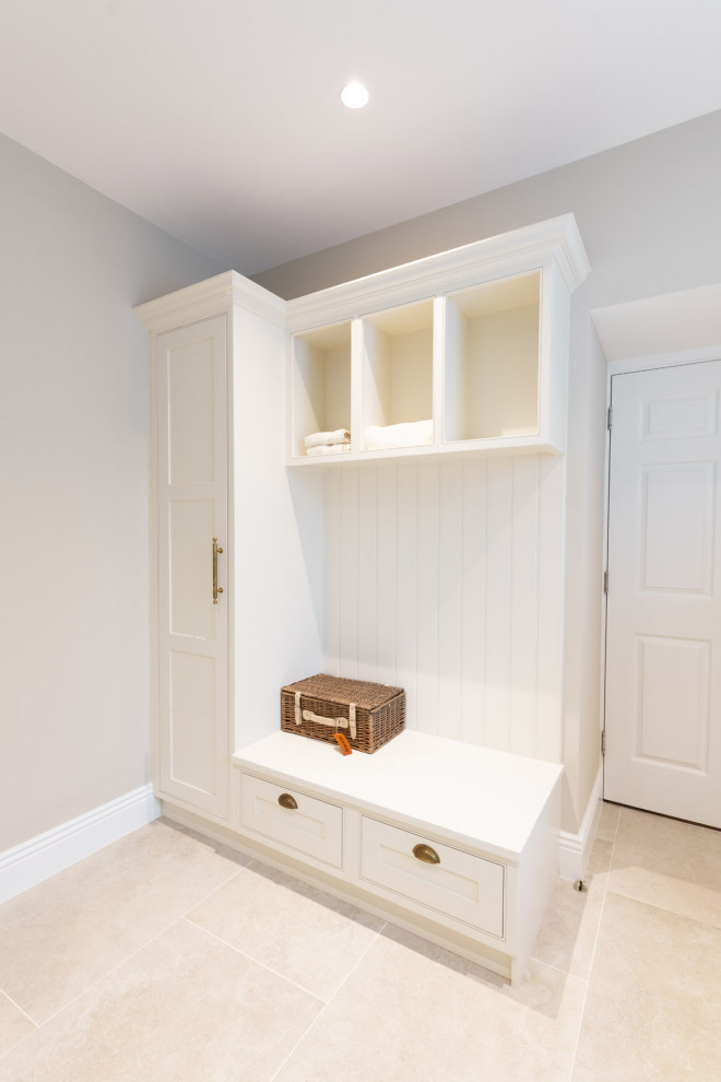 Large classic galley utility room in Hertfordshire with a belfast sink, shaker cabinets, white cabinets, quartz worktops, white walls, ceramic flooring, an integrated washer and dryer, beige floors, white worktops and a feature wall.