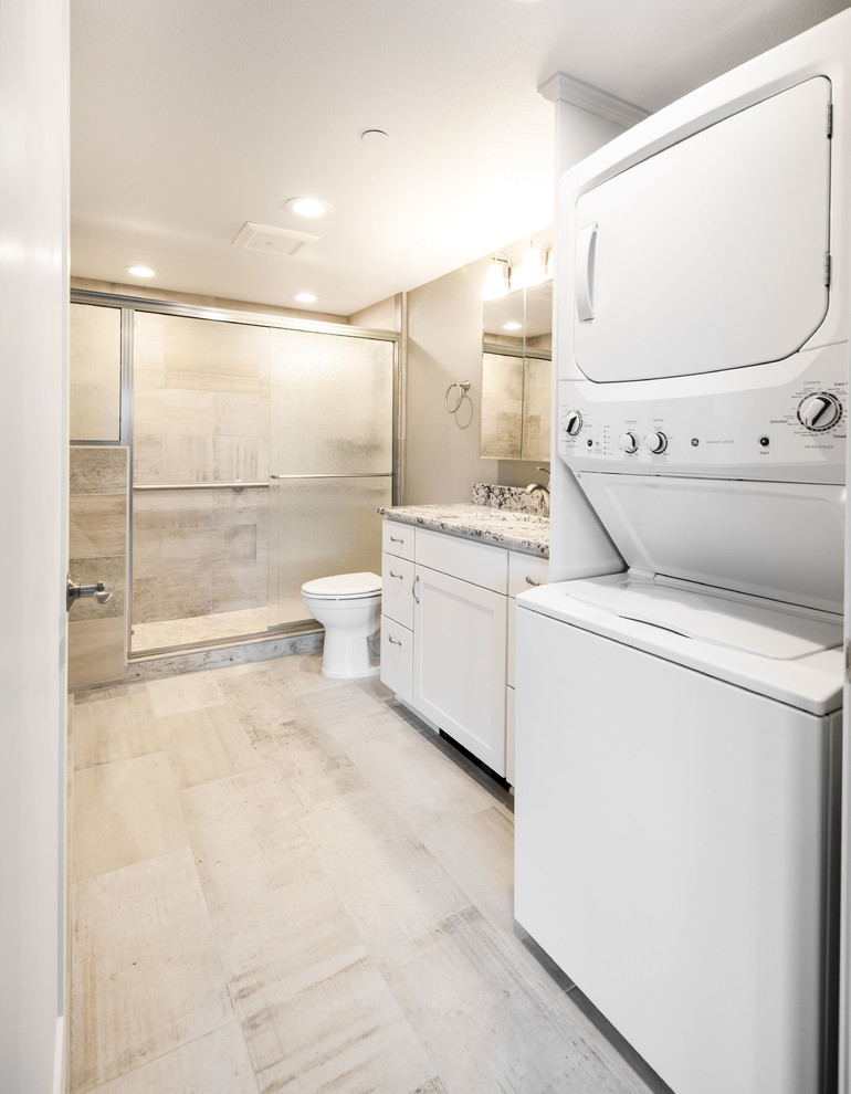 Photo of a mid-sized transitional master bathroom with shaker cabinets, white cabinets, an alcove shower, a one-piece toilet, gray tile, ceramic tile, beige walls, ceramic floors, an undermount sink, granite benchtops, grey floor, a sliding shower screen, multi-coloured benchtops and a laundry.