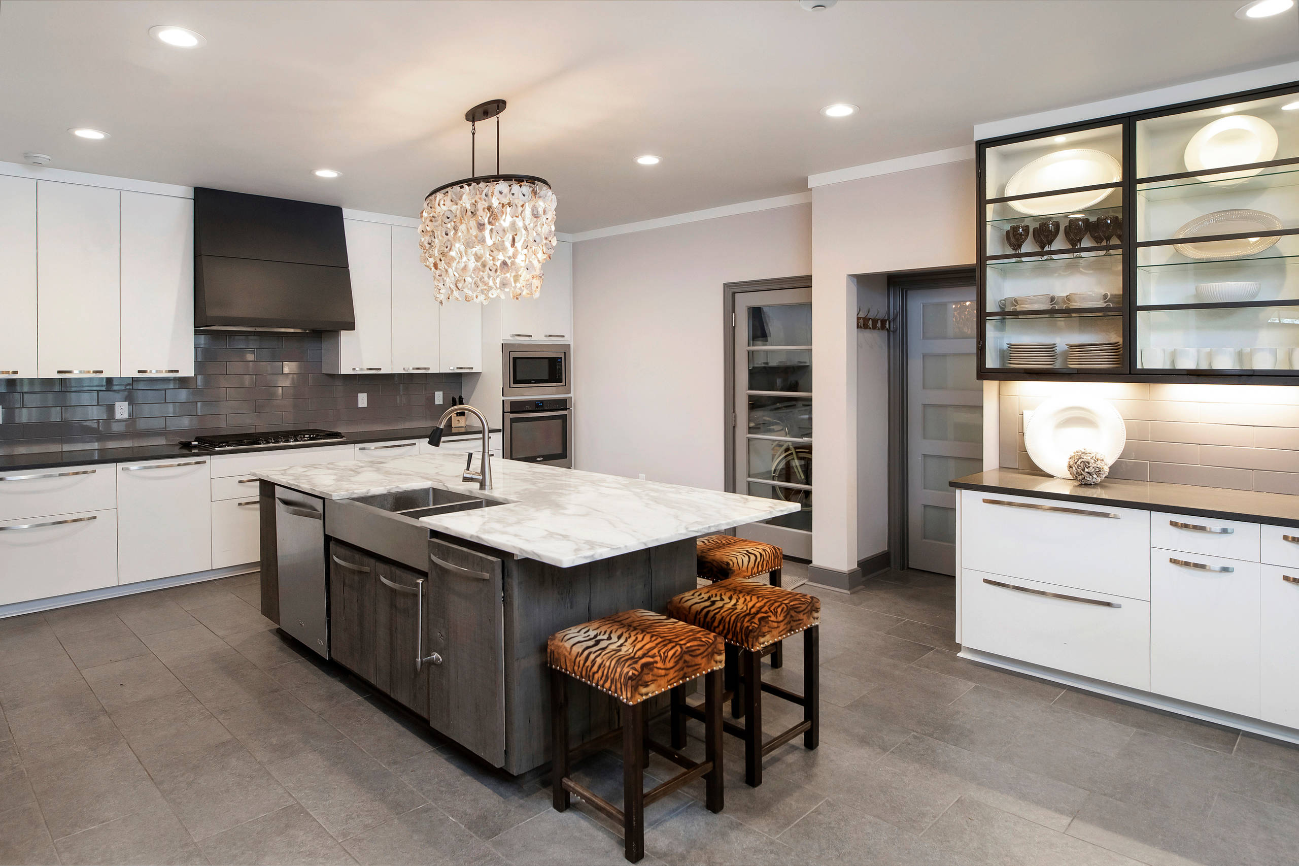 Example of a large u-shaped gray floor kitchen design with a farmhouse sink, flat-panel cabinets, white cabinets, gray backsplash, subway tile backsplash, stainless steel appliances, an island and gra