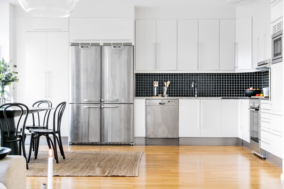 Photo of a large scandinavian l-shaped eat-in kitchen in Stockholm with flat-panel cabinets, white cabinets, black splashback, stainless steel appliances, medium hardwood floors and no island.