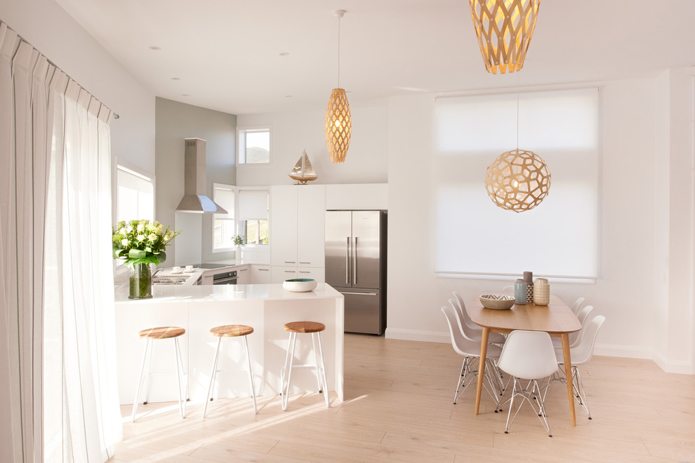 Mid-sized scandinavian u-shaped eat-in kitchen in Other with a double-bowl sink, flat-panel cabinets, white cabinets, quartz benchtops, white splashback, stainless steel appliances, light hardwood floors and no island.