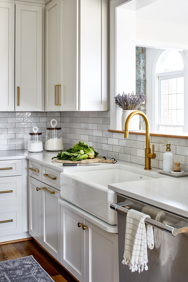 Inspiration for a mid-sized transitional l-shaped separate kitchen in DC Metro with a farmhouse sink, shaker cabinets, white cabinets, quartz benchtops, grey splashback, ceramic splashback, stainless steel appliances, light hardwood floors, with island and white benchtop.