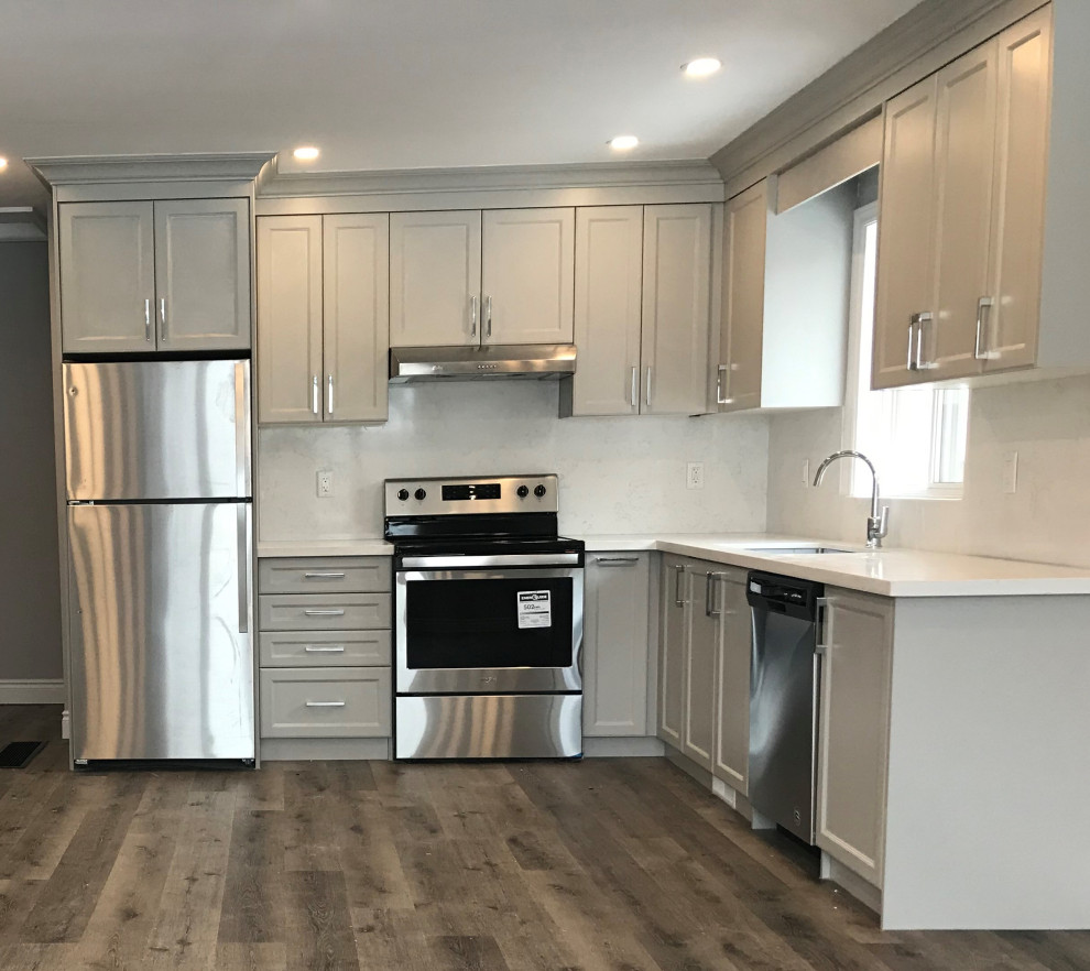 Example of a mid-sized transitional l-shaped medium tone wood floor kitchen design with an undermount sink, shaker cabinets, gray cabinets, quartz countertops, quartz backsplash, stainless steel appliances and white countertops