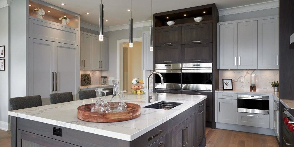 Example of a large transitional l-shaped medium tone wood floor and brown floor kitchen design in Miami with an undermount sink, shaker cabinets, gray cabinets, marble countertops, white backsplash, stone slab backsplash, stainless steel appliances and an island