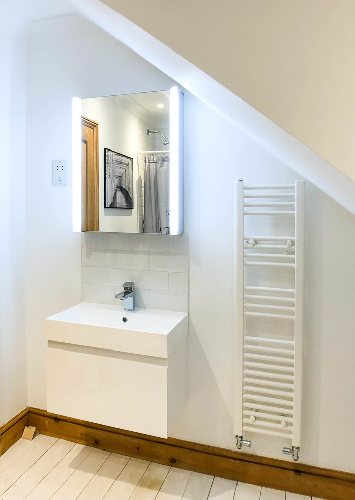 This is an example of a large scandinavian kids bathroom in Berkshire with glass-front cabinets, grey cabinets, a drop-in tub, a shower/bathtub combo, a one-piece toilet, gray tile, ceramic tile, white walls, painted wood floors, an integrated sink, white floor and a sliding shower screen.