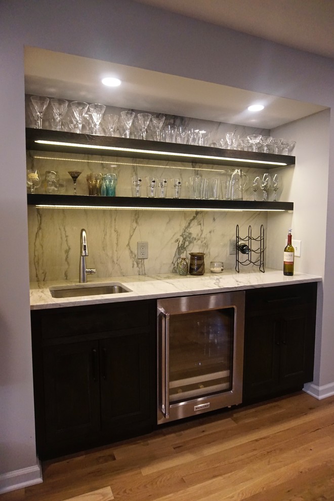 Inspiration for a large transitional medium tone wood floor home bar remodel in Indianapolis with an undermount sink, beaded inset cabinets, dark wood cabinets, quartzite countertops, white backsplash, stone slab backsplash, stainless steel appliances and an island