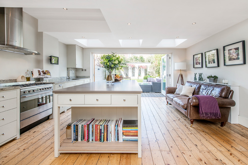 Photo of a large transitional single-wall open plan kitchen in London with flat-panel cabinets, white cabinets, stainless steel appliances, medium hardwood floors, with island, an undermount sink, granite benchtops and grey splashback.