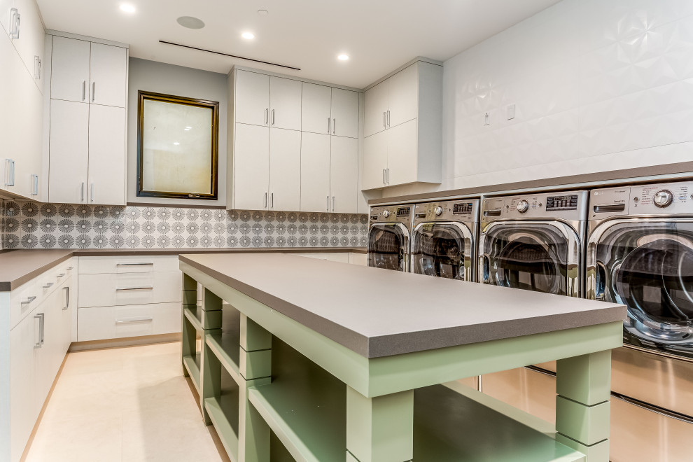 Idéer för en stor modern grå parallell tvättstuga enbart för tvätt, med en tvättmaskin och torktumlare bredvid varandra, släta luckor, vita skåp, bänkskiva i kvarts, flerfärgad stänkskydd, stänkskydd i porslinskakel, vita väggar, kalkstensgolv och beiget golv