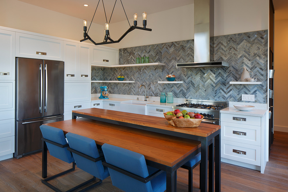 Photo of a mid-sized country l-shaped eat-in kitchen in San Francisco with a farmhouse sink, shaker cabinets, white cabinets, quartzite benchtops, blue splashback, glass tile splashback, stainless steel appliances, medium hardwood floors and with island.