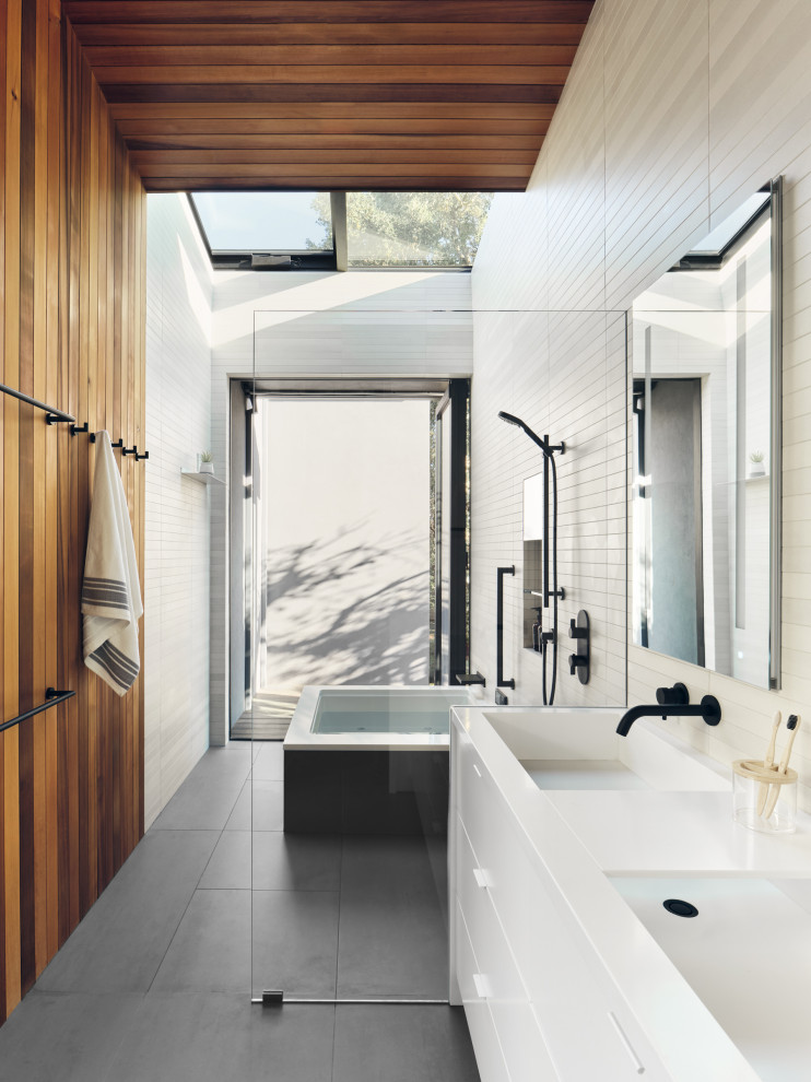 Inspiration för stora moderna vitt en-suite badrum, med släta luckor, vita skåp, ett undermonterat badkar, våtrum, en vägghängd toalettstol, beige kakel, porslinskakel, beige väggar, klinkergolv i porslin, ett avlångt handfat, bänkskiva i akrylsten, grått golv och med dusch som är öppen