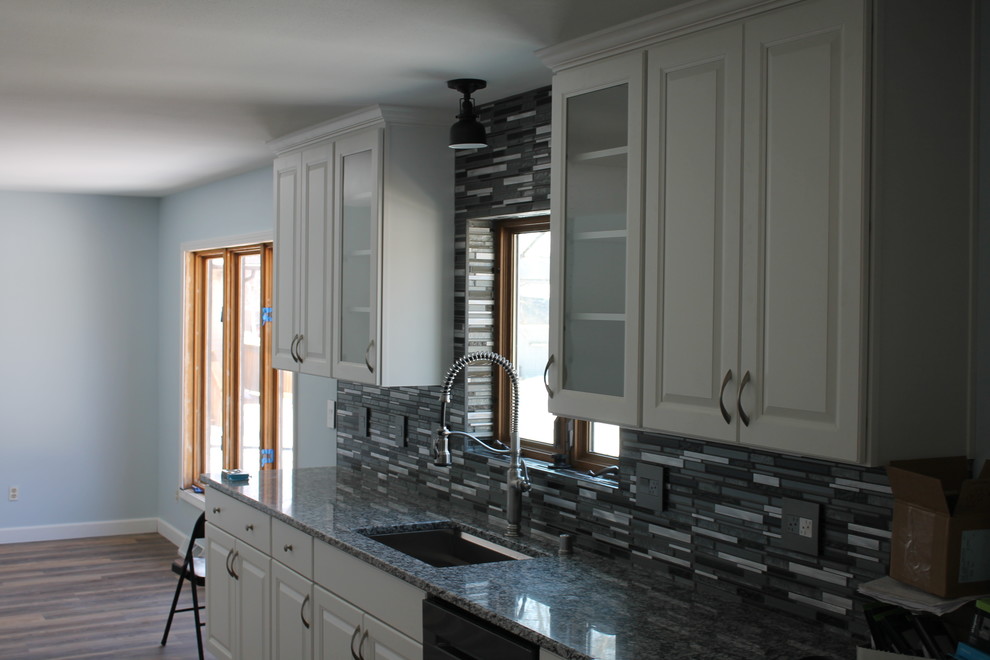 Inspiration for a mid-sized transitional u-shaped dark wood floor and brown floor kitchen remodel with an undermount sink, raised-panel cabinets, white cabinets, granite countertops, multicolored backsplash, matchstick tile backsplash, stainless steel appliances and an island