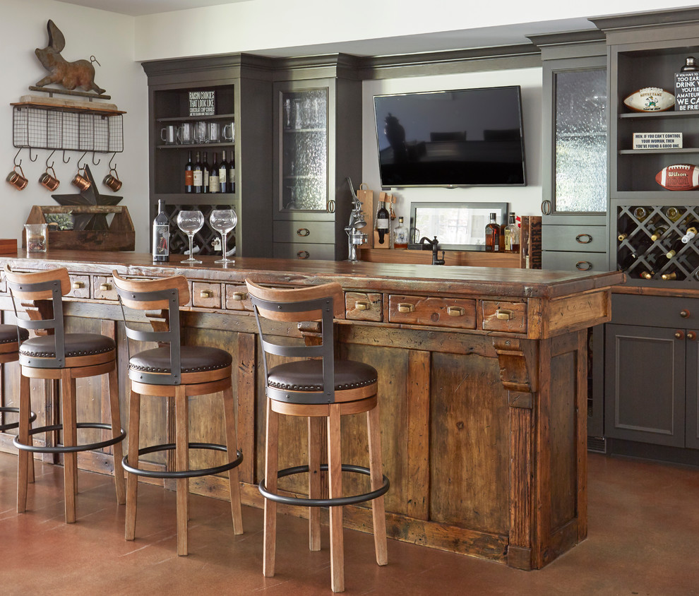 This is an example of a large country galley wet bar in Chicago with recessed-panel cabinets, grey cabinets, wood benchtops, brown floor, brown benchtop and concrete floors.