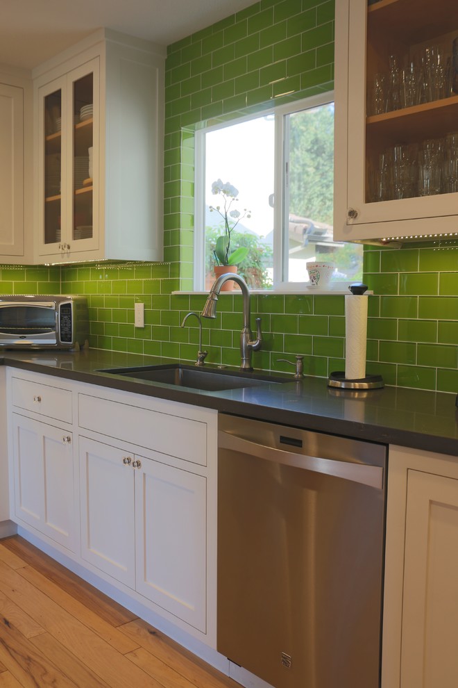 Photo of a mid-sized country u-shaped eat-in kitchen in San Luis Obispo with shaker cabinets, white cabinets, quartz benchtops, green splashback, glass tile splashback, stainless steel appliances, an undermount sink, light hardwood floors, no island, brown floor and grey benchtop.