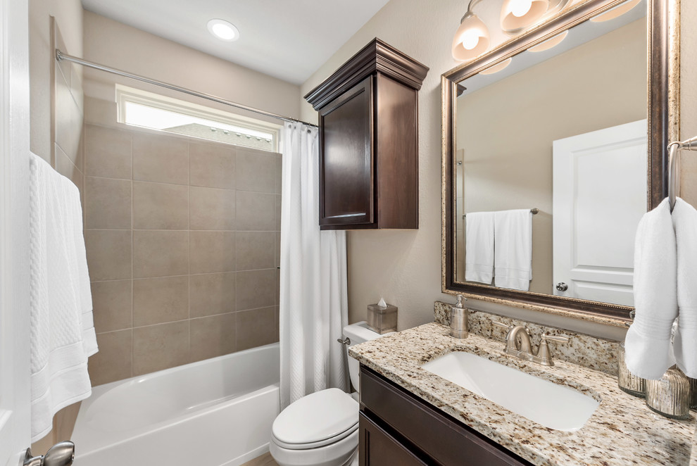 Mid-sized arts and crafts kids bathroom in Austin with recessed-panel cabinets, dark wood cabinets, an alcove tub, a shower/bathtub combo, a two-piece toilet, beige tile, ceramic tile, grey walls, vinyl floors, an undermount sink, granite benchtops, brown floor, a shower curtain and beige benchtops.