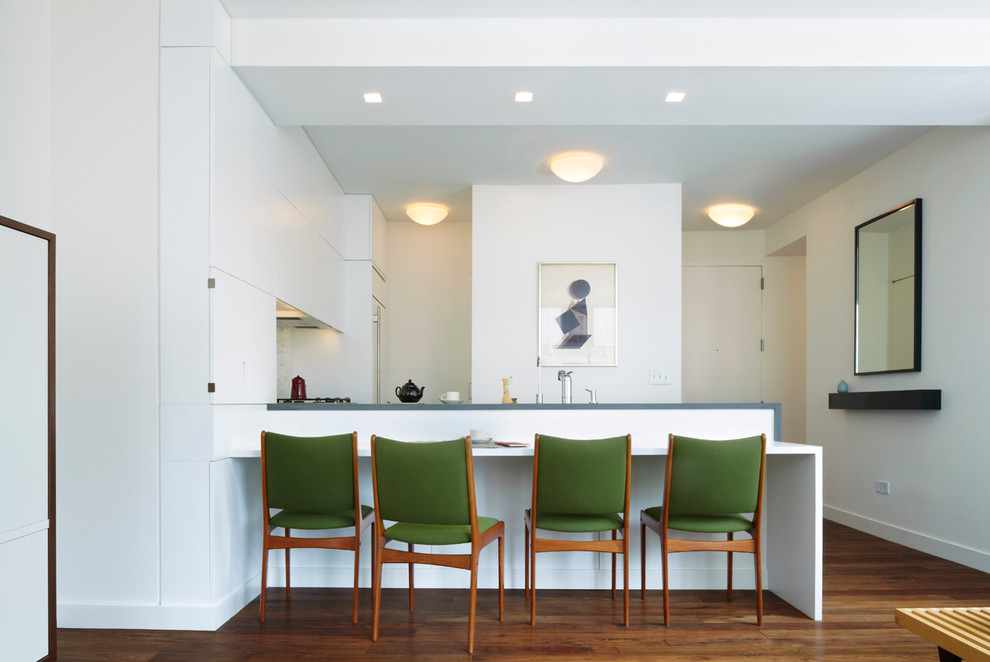 Photo of a small modern eat-in kitchen in New York with an undermount sink, flat-panel cabinets, white cabinets, limestone benchtops, white splashback, stone tile splashback, panelled appliances, medium hardwood floors and a peninsula.