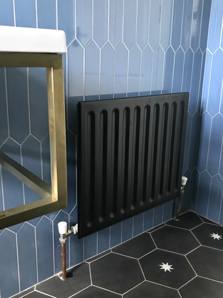 Modern inredning av ett litet vit vitt en-suite badrum, med öppna hyllor, en toalettstol med separat cisternkåpa, blå kakel, keramikplattor, blå väggar, cementgolv, ett väggmonterat handfat, bänkskiva i akrylsten och svart golv