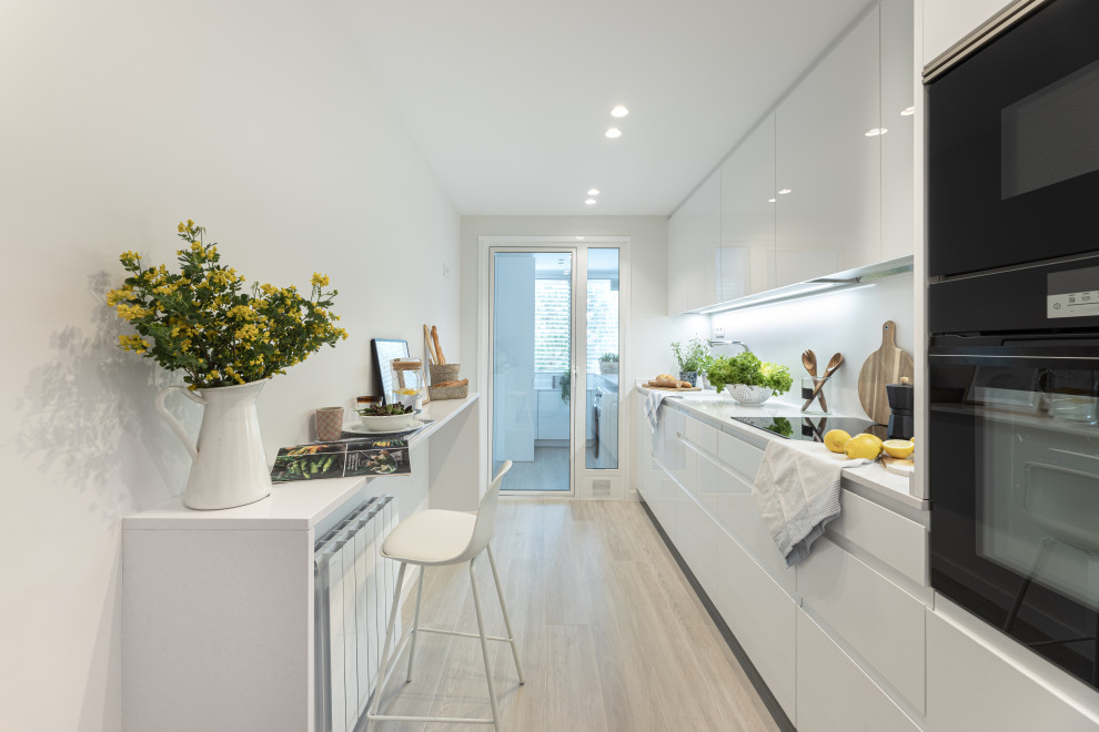 This is an example of a mid-sized contemporary single-wall separate kitchen in Barcelona with an undermount sink, white cabinets, quartz benchtops, white splashback, engineered quartz splashback, black appliances, ceramic floors, no island, beige floor, white benchtop and flat-panel cabinets.