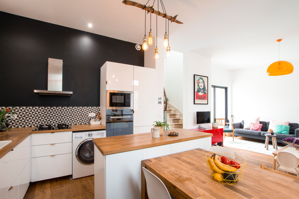 Photo of a small eclectic l-shaped open plan kitchen in Bordeaux with flat-panel cabinets, wood benchtops, black splashback, ceramic splashback, dark hardwood floors and with island.