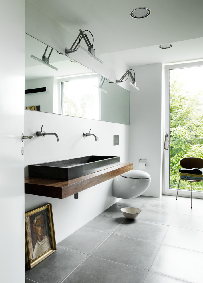 Photo of a large scandinavian master bathroom in Aarhus with a trough sink, wood benchtops, a wall-mount toilet, white walls, white tile, cement tile, ceramic floors and brown benchtops.