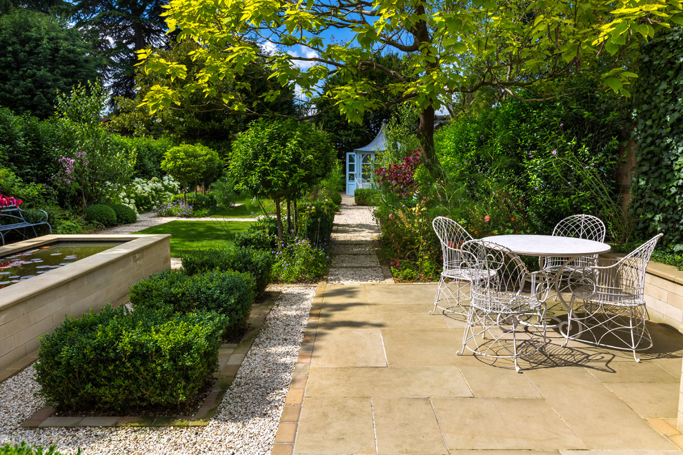 This is an example of a mid-sized traditional backyard patio in London with natural stone pavers.