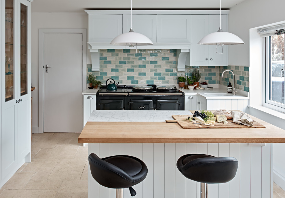 Photo of a small transitional kitchen in Wiltshire with blue cabinets, porcelain splashback, black appliances, an undermount sink, shaker cabinets, wood benchtops, multi-coloured splashback, with island and beige floor.