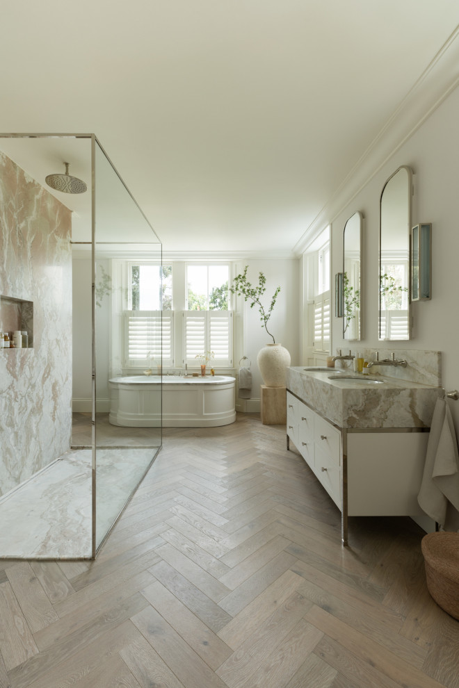 Traditional ensuite bathroom in London with flat-panel cabinets, white cabinets, a freestanding bath, a built-in shower, white walls, light hardwood flooring, a submerged sink, beige floors, an open shower, grey worktops, double sinks and a freestanding vanity unit.