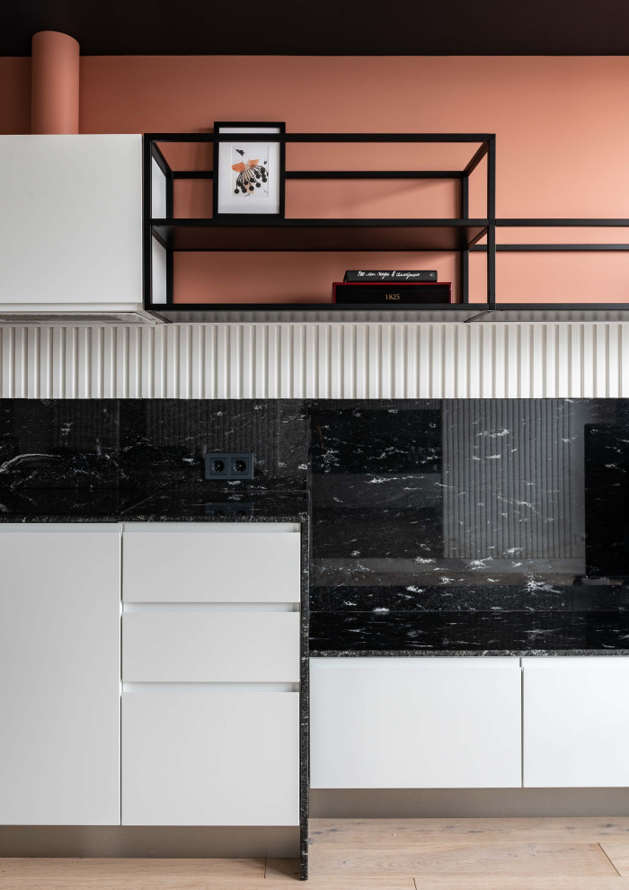 Photo of a small scandinavian single-wall eat-in kitchen in Moscow with an undermount sink, flat-panel cabinets, white cabinets, granite benchtops, black splashback, granite splashback, black appliances, with island and black benchtop.