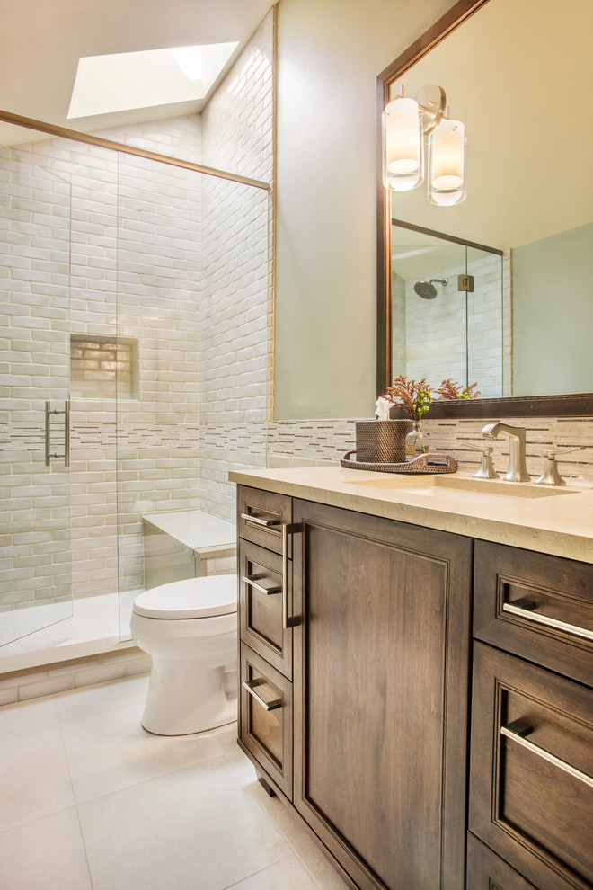 Photo of a mid-sized country 3/4 bathroom in Denver with an undermount sink, recessed-panel cabinets, dark wood cabinets, solid surface benchtops, an alcove shower, a one-piece toilet, beige tile, ceramic tile, beige walls, ceramic floors, white floor and a hinged shower door.