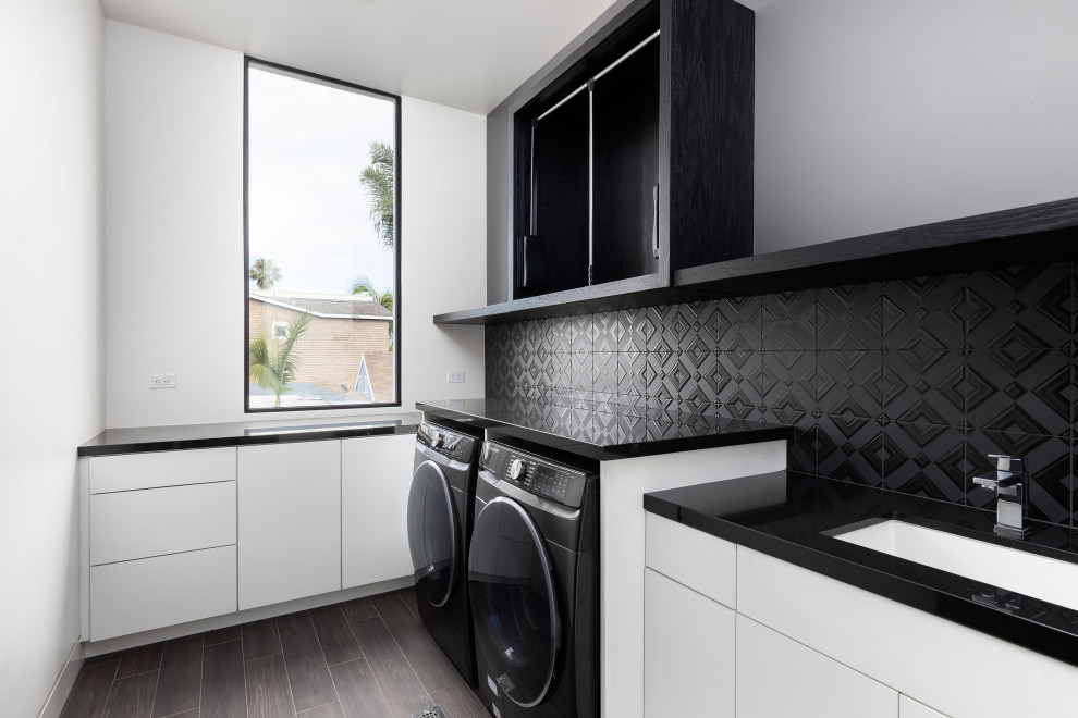 Example of a small trendy beige floor dedicated laundry room design in San Diego with an integrated sink, white backsplash, white walls, a side-by-side washer/dryer and black countertops