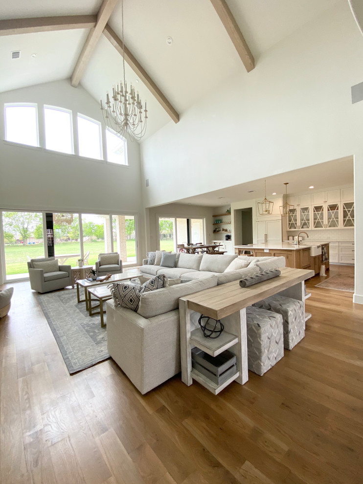 Expansive scandinavian open concept family room in Dallas with white walls, light hardwood floors, a stone fireplace surround, a wall-mounted tv, beige floor and exposed beam.