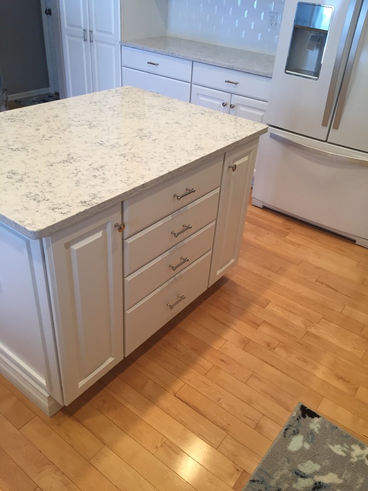 Large transitional u-shaped light wood floor and beige floor open concept kitchen photo in Denver with a farmhouse sink, raised-panel cabinets, white cabinets, quartz countertops, white backsplash, ceramic backsplash, white appliances and an island