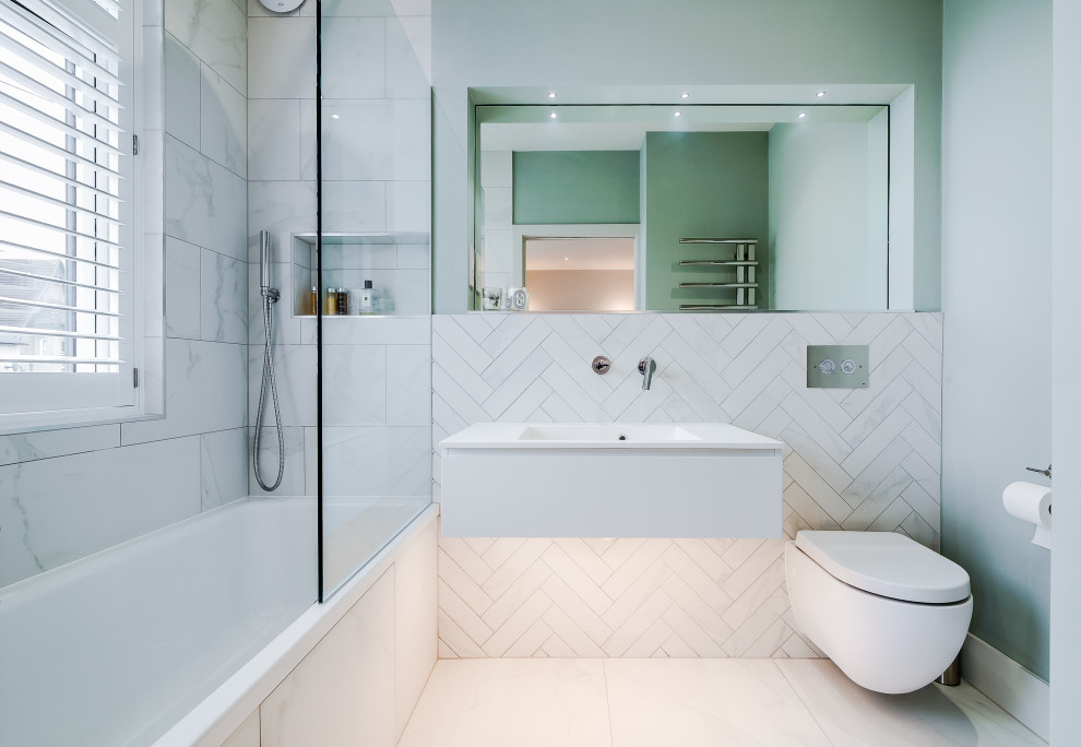 This is an example of a mid-sized contemporary 3/4 bathroom in London with flat-panel cabinets, white cabinets, an alcove shower, a wall-mount toilet, white tile, porcelain tile, green walls, porcelain floors, an integrated sink, white floor and white benchtops.