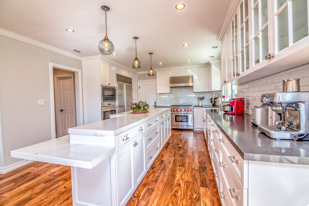 This is an example of a large contemporary u-shaped eat-in kitchen in San Francisco with a farmhouse sink, shaker cabinets, white cabinets, marble benchtops, white splashback, subway tile splashback, stainless steel appliances, medium hardwood floors and with island.