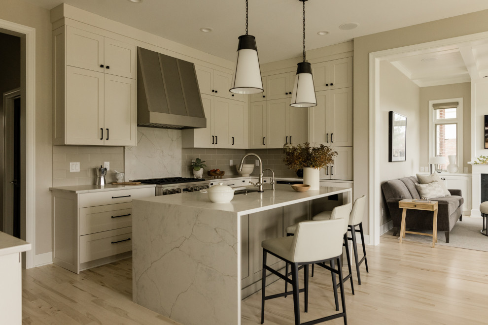 Example of a mid-sized transitional u-shaped light wood floor eat-in kitchen design with an undermount sink, recessed-panel cabinets, beige cabinets, quartz countertops, gray backsplash, ceramic backsplash, stainless steel appliances, an island and white countertops
