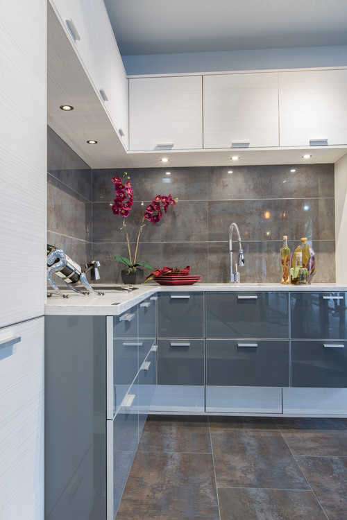 Modern L-shaped kitchen with textured white wood-grain upper cabinets, glossy gray slab lowers, LED under-cabinet lighting, quartz countertop, and large tile backsplash